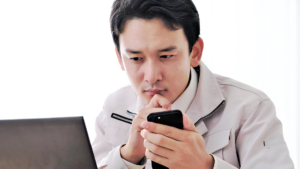スマホを持ちながらパソコンを見つめる男性